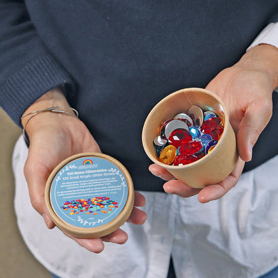 Set of 100 Grimms small acrylic glitter stones in assorted colours inside a palm leaf shell, shimmering loose parts for creative play