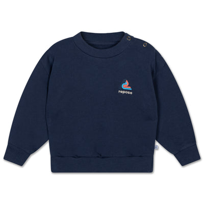 Nightshade blue organic cotton baby crewneck sweater with branded chest embroidery. Features ribbed neck, cuffs, and hem, plus snap button closure on smaller sizes for easy dressing. Soft, breathable, and designed for durability