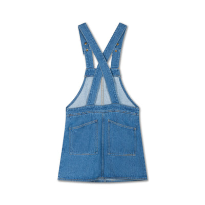 Medium blue dungaree dress made from durable organic cotton denim. Features adjustable snap-button shoulder straps, front and back patch pockets, A-line skirt, embroidered logo, and woven brand tag.