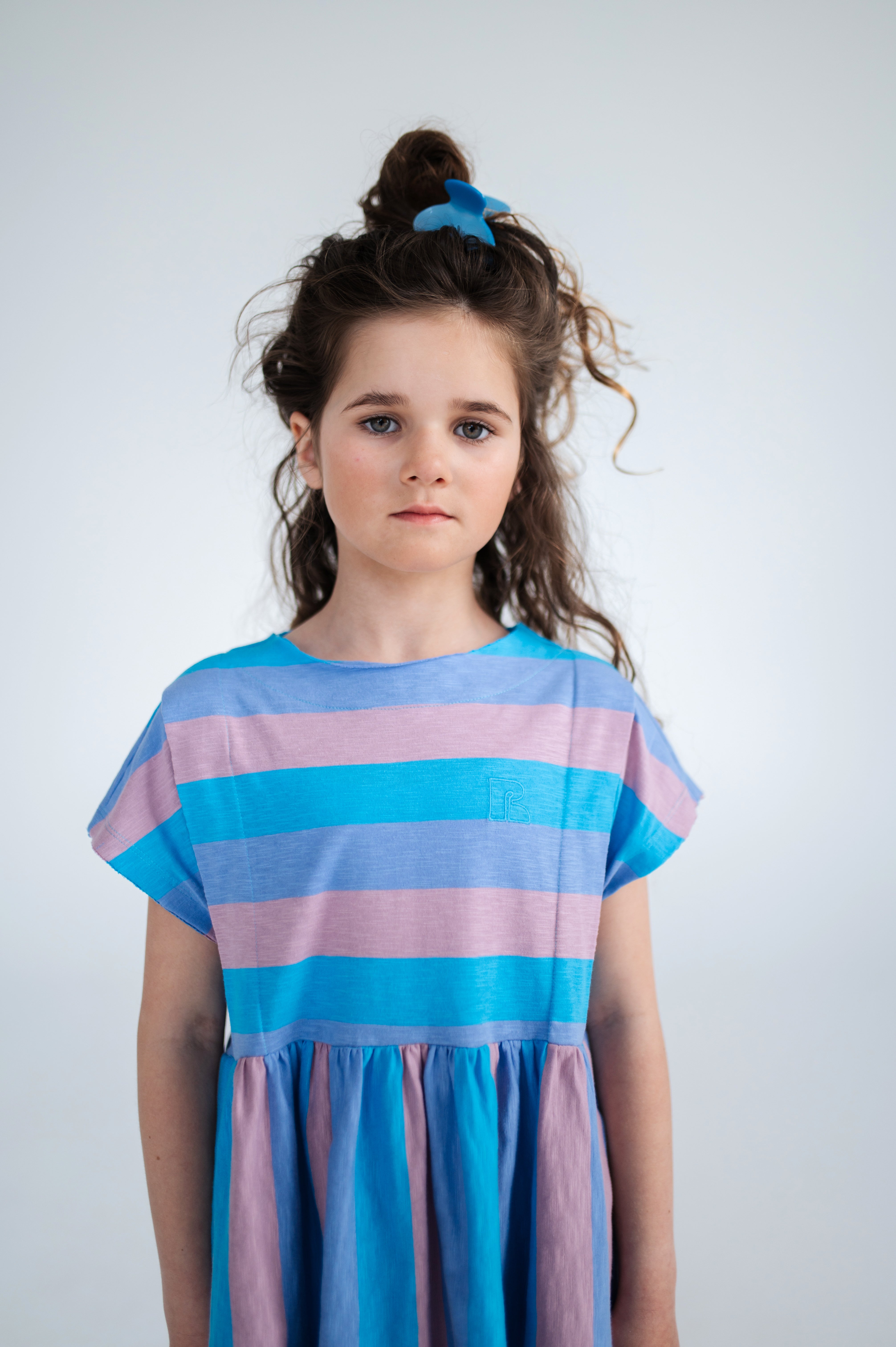 Tricolor block stripe dress made from 100% yarn-dyed organic cotton flamé. Features pleated front details, ruffled waist, side pockets, short sleeves, and raw edge neckline. A lightweight and comfortable dress for everyday wear.